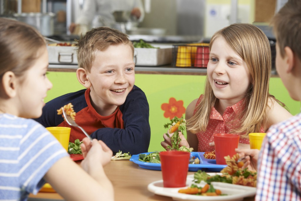 Group Of Pupils Sitting At Table In School Cafeteria Eating Lunc